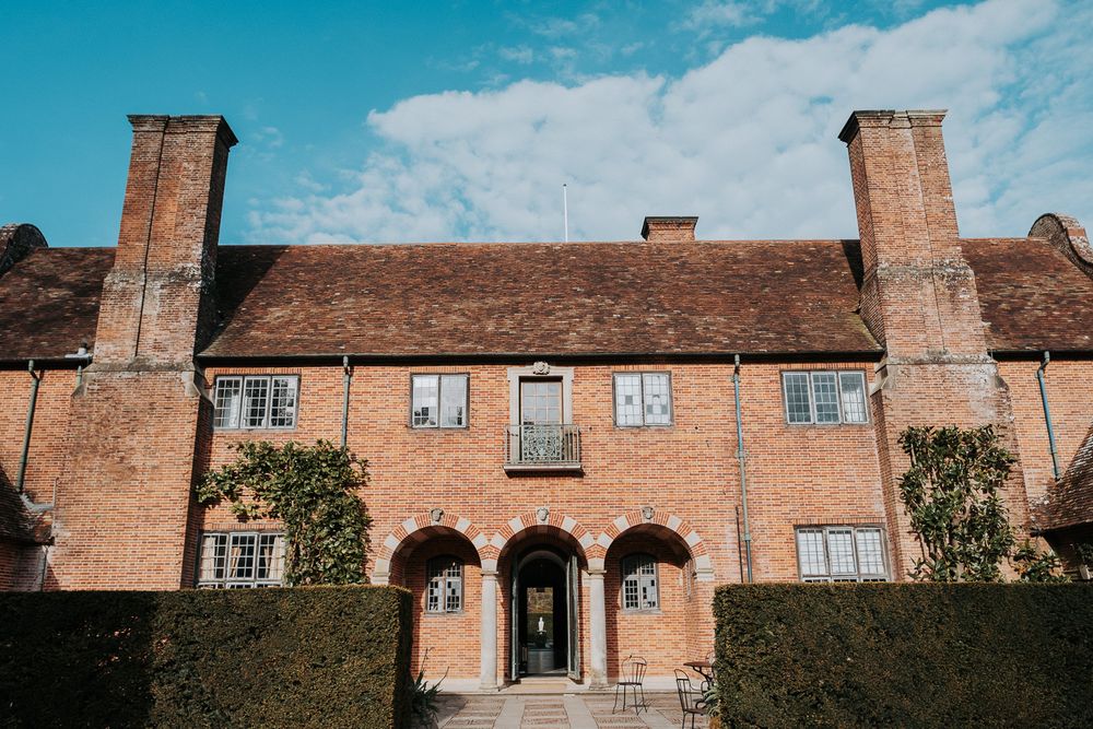 Historic red brick almshouse buildings with Tudor-style architecture and arched entryways line a traditional courtyard.