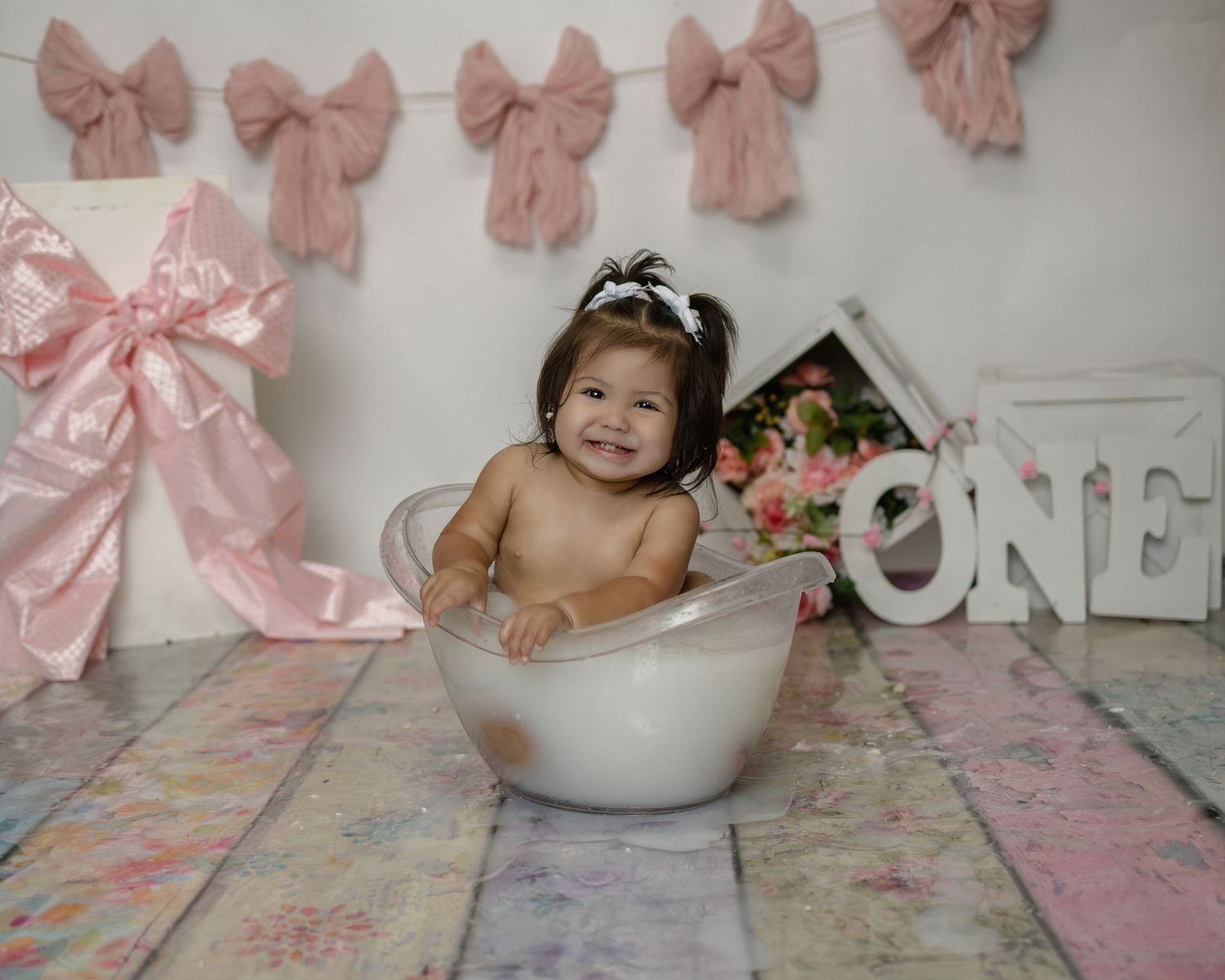Pink bows and decorative elements adorn a wall in a nursery-themed photo session setup.