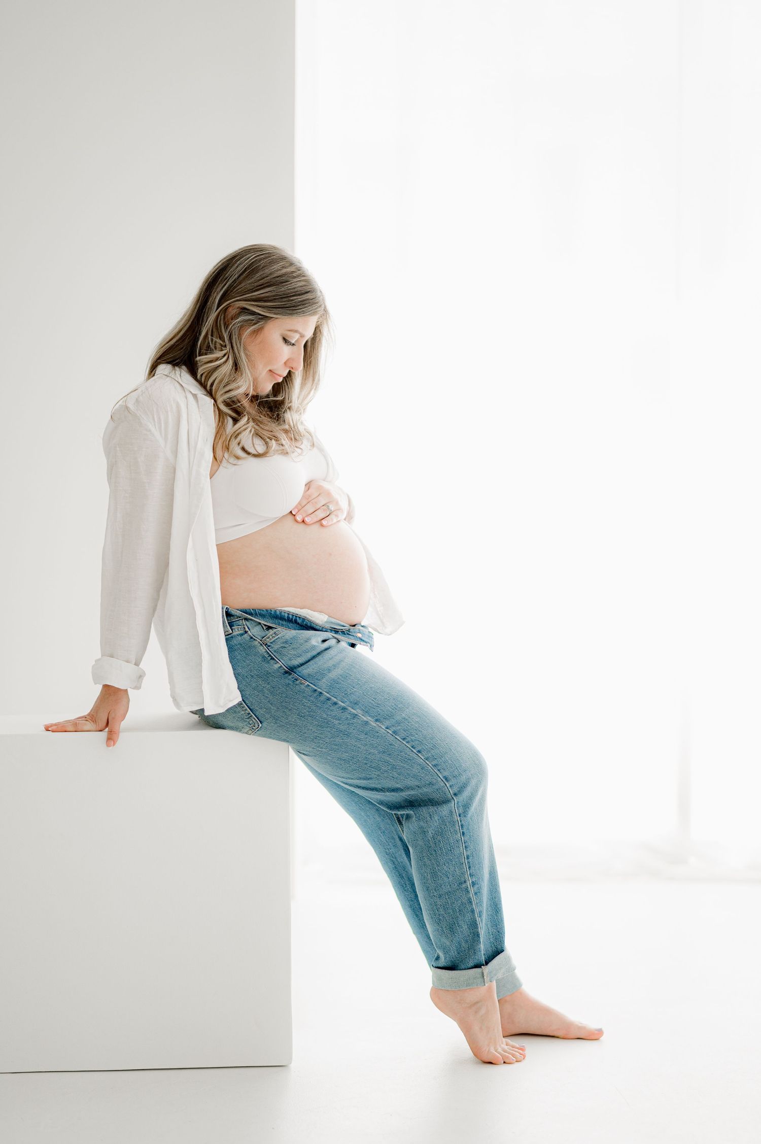 Expectant mother in jeans and white top with belly out during  Jacksonville, FL maternity photography session.