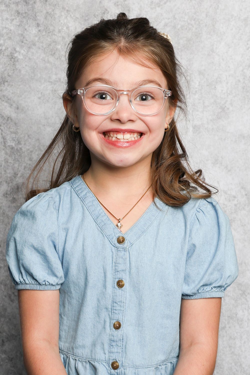 Student wearing glasses and light blue button-up dress with puff sleeves against gray backdrop.