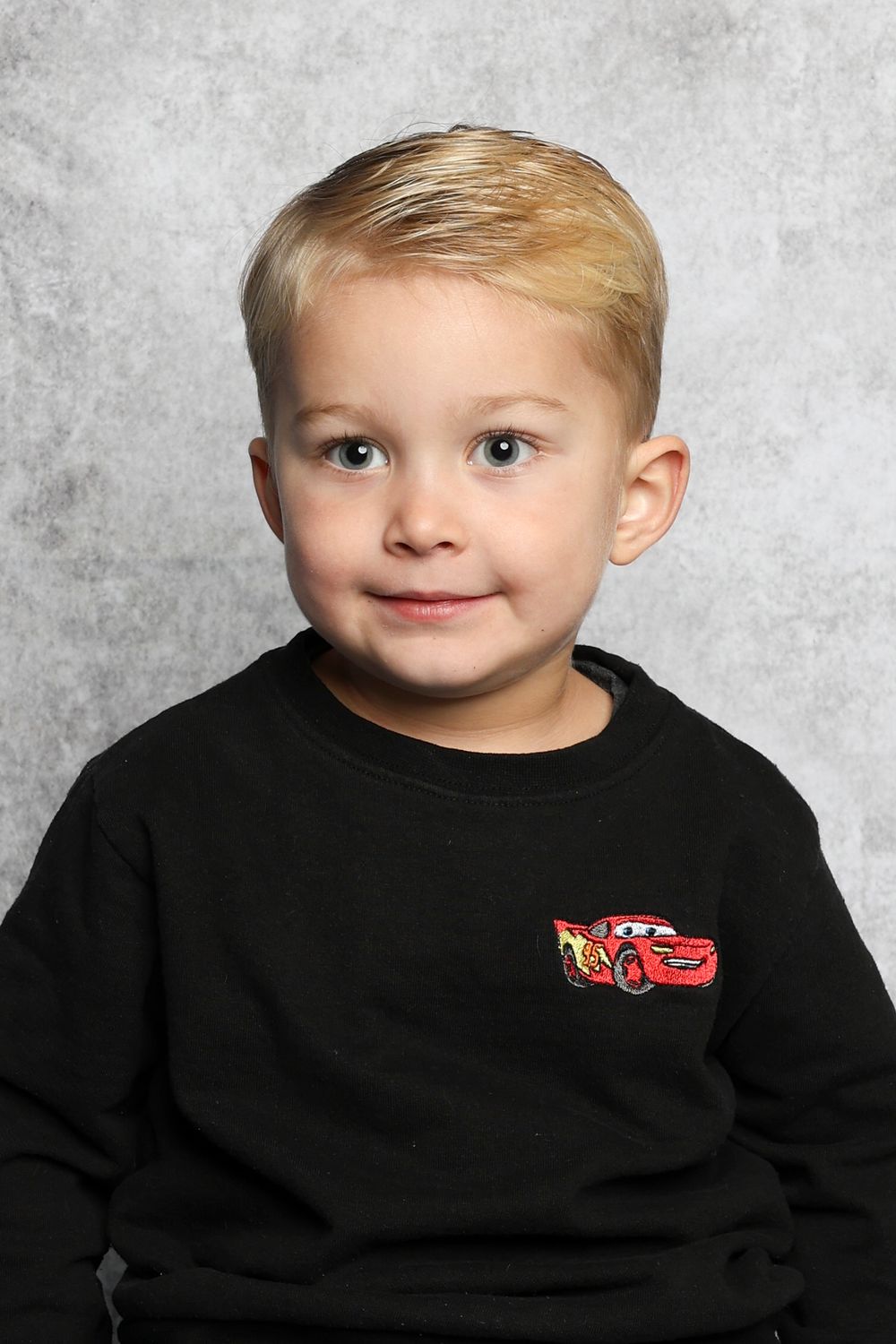 Young child in black sweatshirt with Cars character logo against gray background.