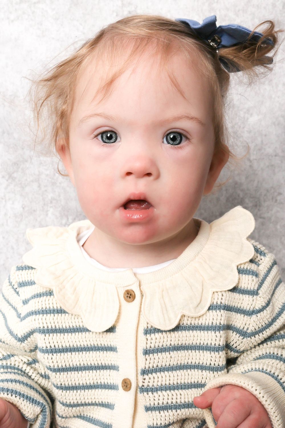 Baby wearing a cream and blue striped sweater with scalloped collar against white background.