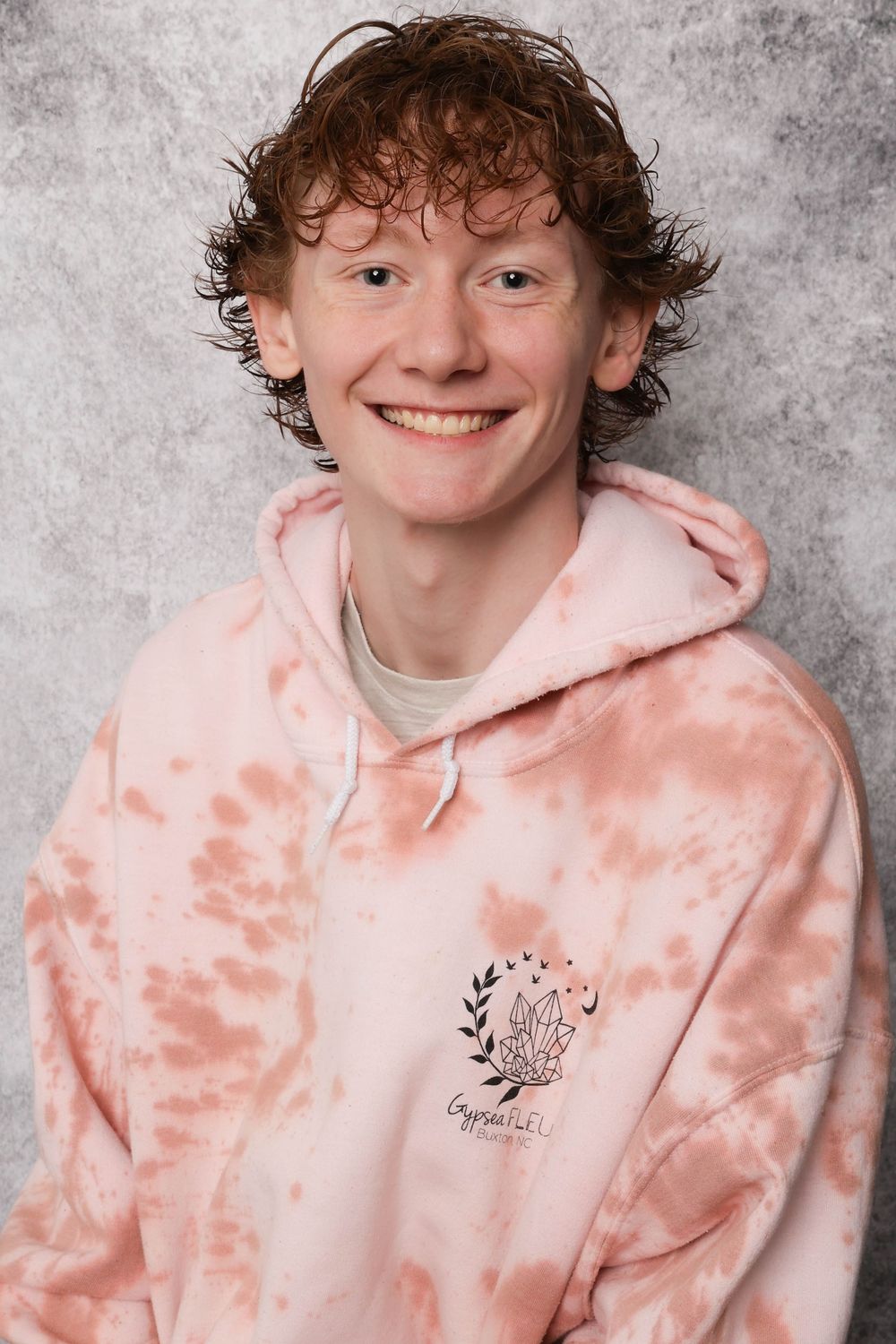Person in pink tie-dye hoodie posing against grey background.