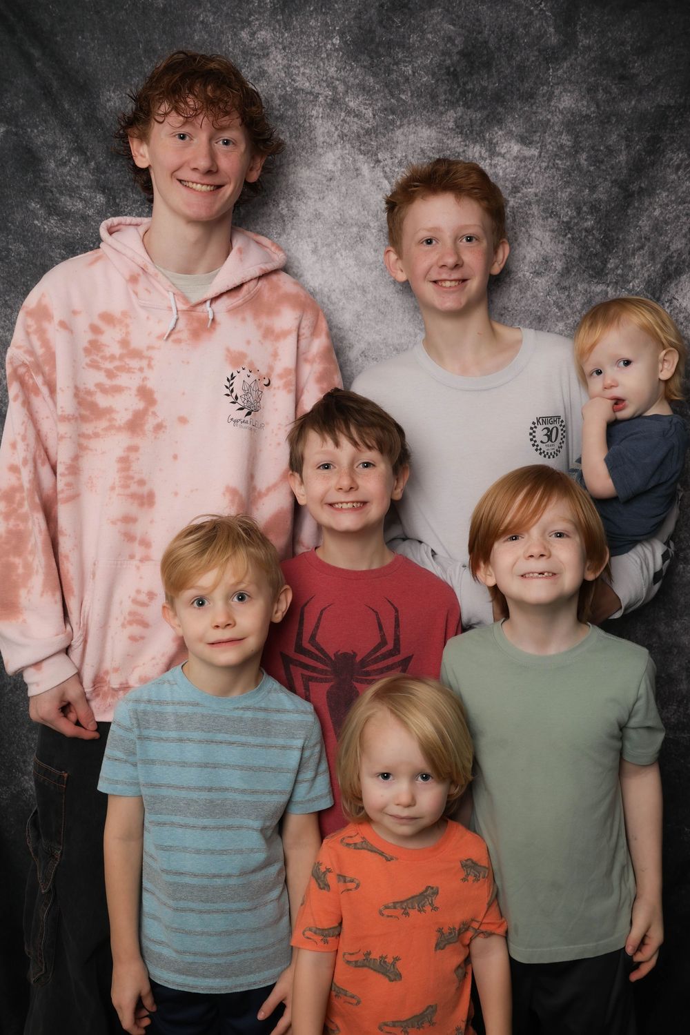 Group photo of siblings wearing casual clothing against grey backdrop.