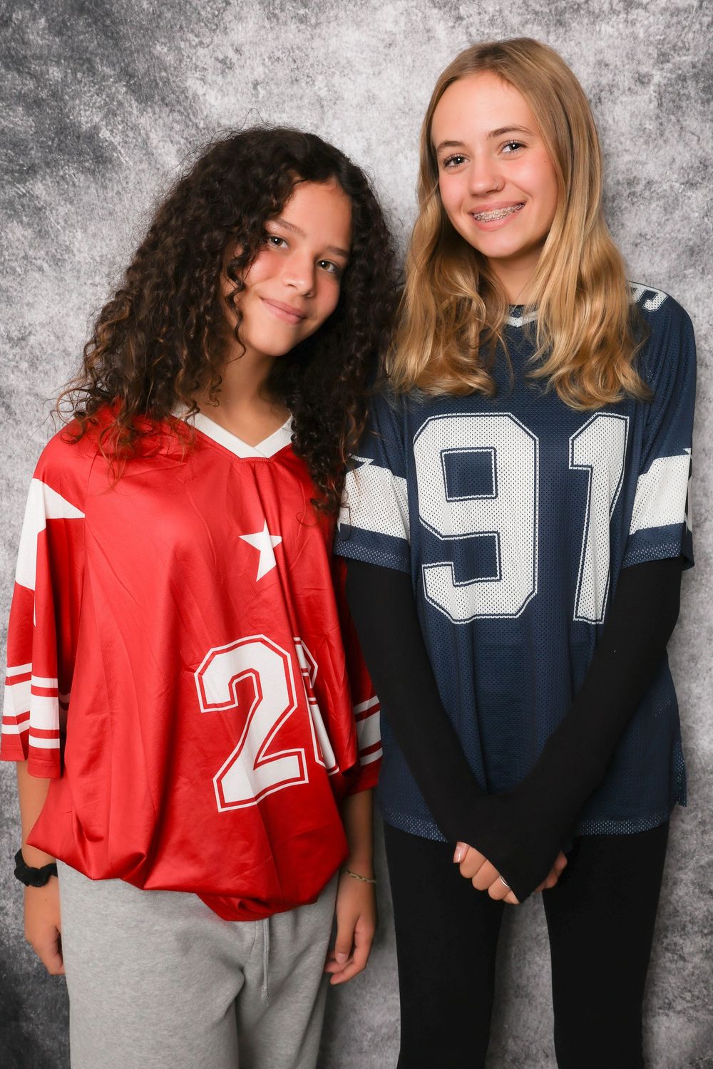 Two students posing in sports jerseys numbered 21 and 91 against a gray backdrop.
