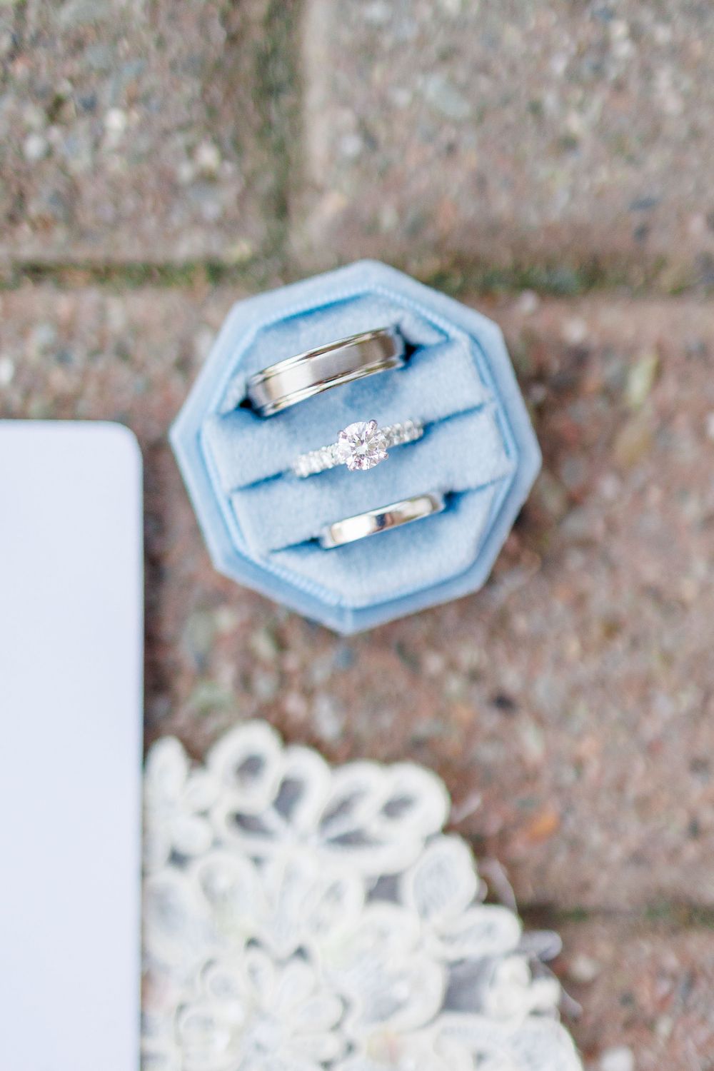 Wedding rings displayed on light blue hexagonal ring holders against a textured brick background.