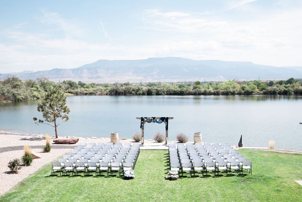 Outdoor lakeside wedding ceremony setup with white chairs and mountain views in the background.