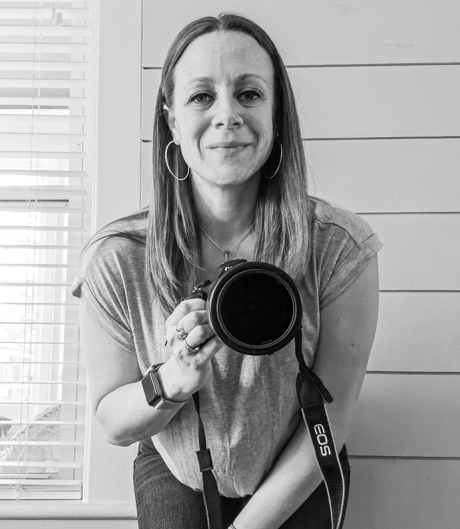 Black and white portrait of a female photographer holding a Canon EOS camera with a large lens.