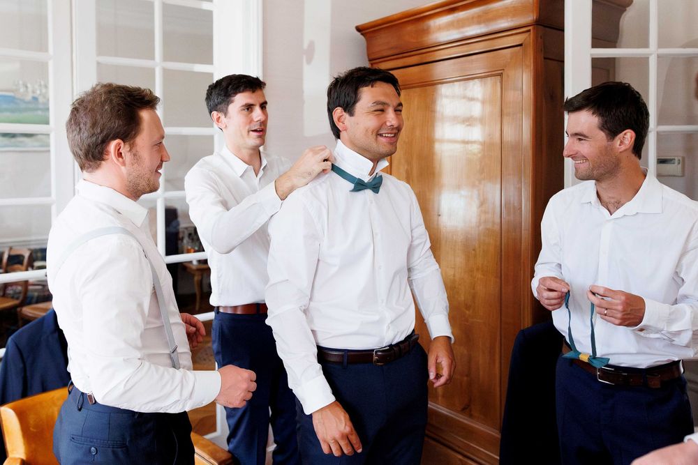 Groomsmen getting ready in formal attire in a wood-paneled room.