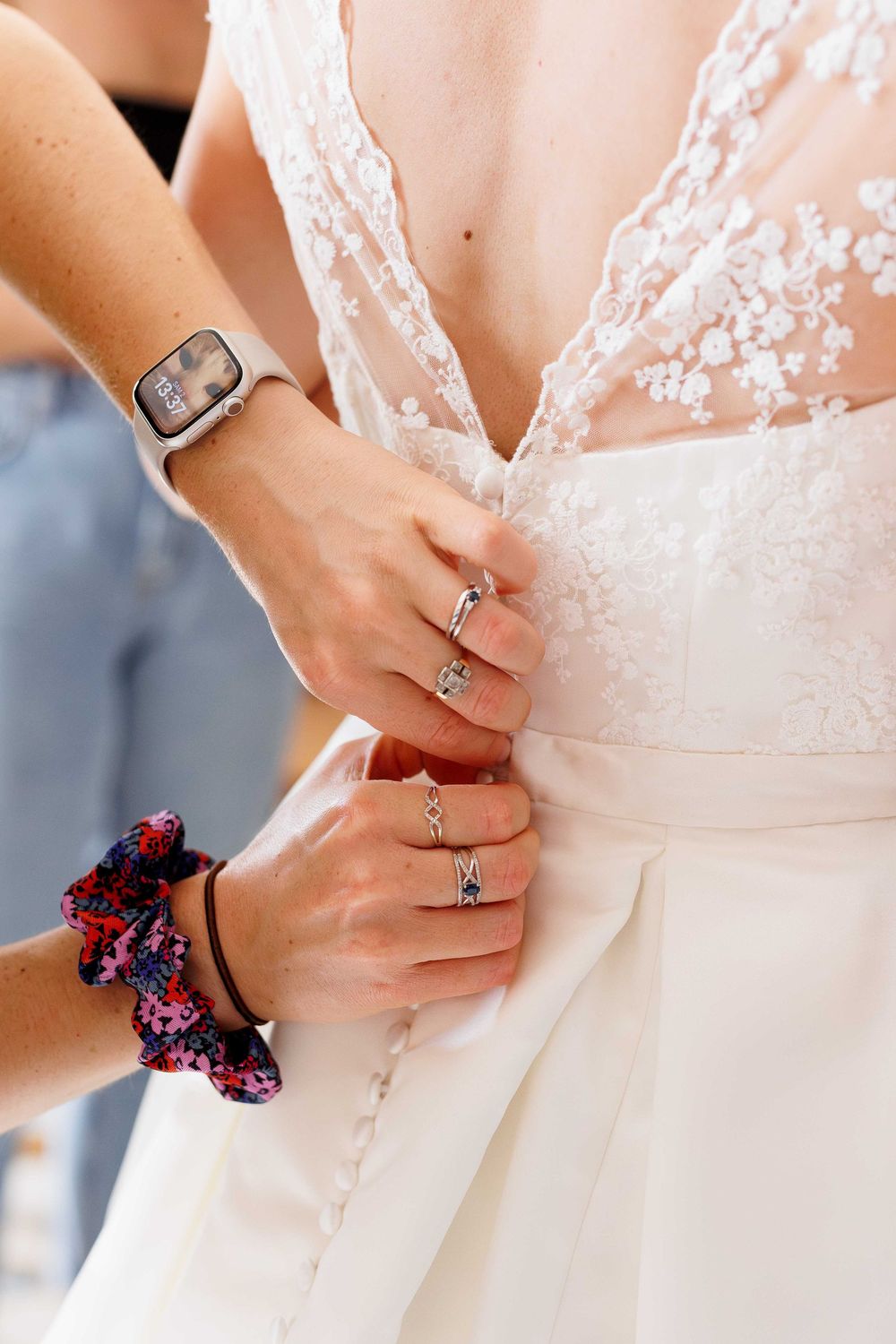 Detailed view of hands fastening back of white lace wedding gown.