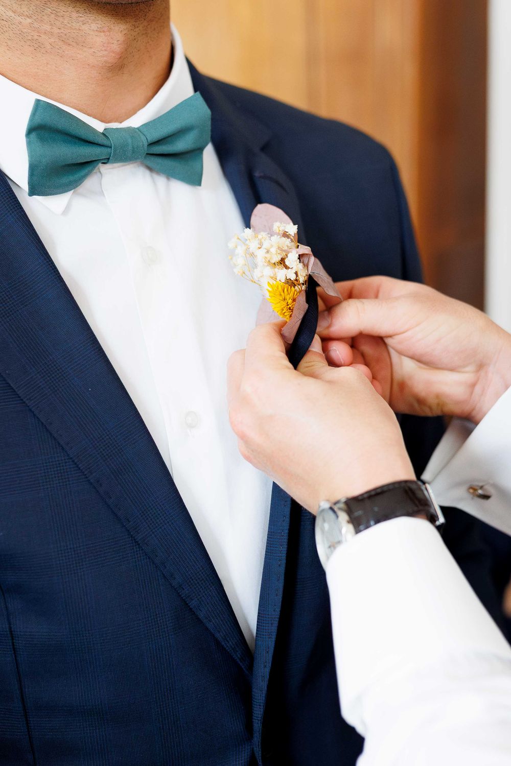 Close-up of teal bowtie and boutonniere being adjusted on navy suit.