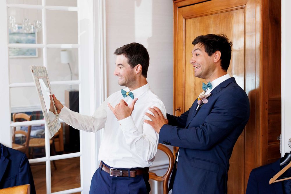 Two men in business suits adjusting formal attire and accessories during wedding preparations.
