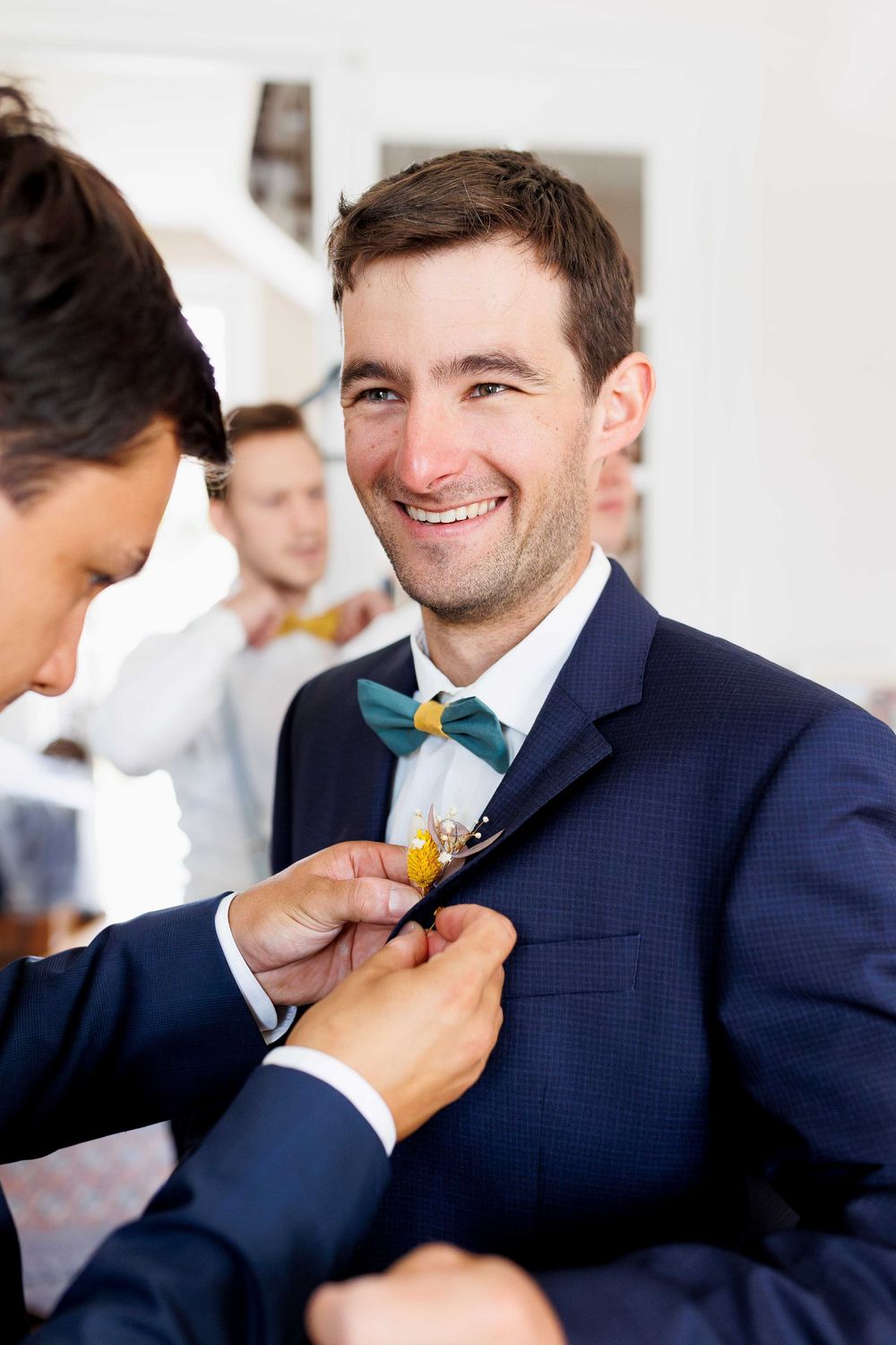 Groomsmen helping adjust yellow boutonniere on navy suit lapel.