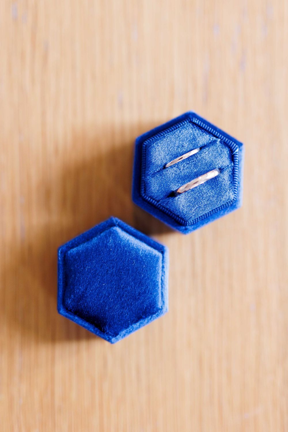 Two blue hexagonal ring boxes arranged on wooden surface.