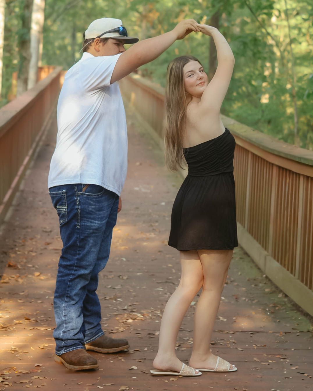 Couple dancing together on a wooden bridge surrounded by trees.