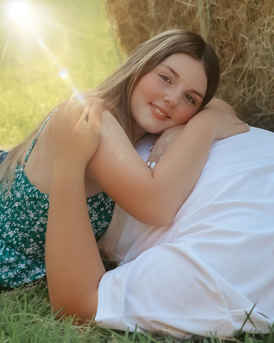 Person in floral dress lying in golden sunlit grass near hay bales.