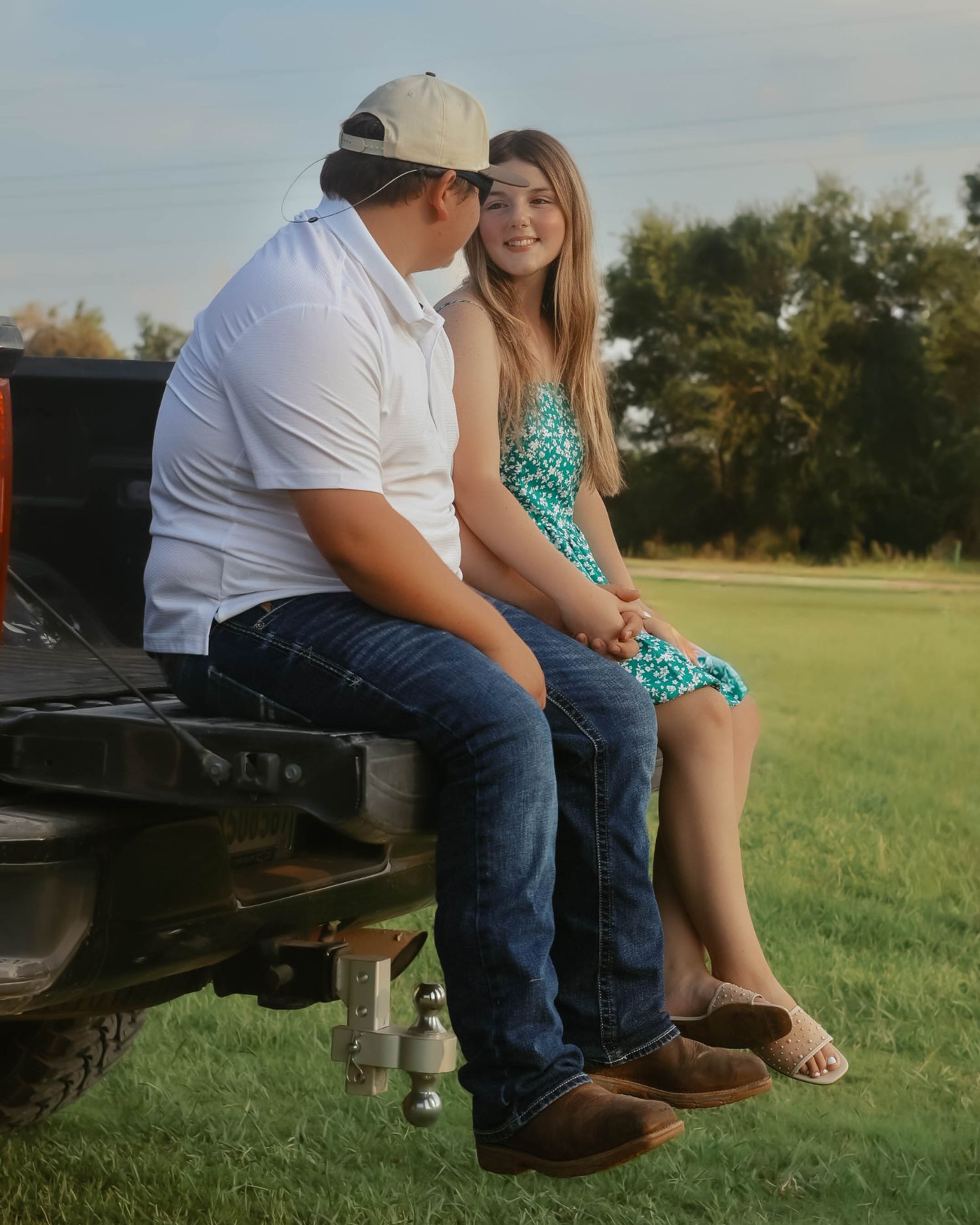 Couple sitting casually on the tailgate of a truck in a sunny field.