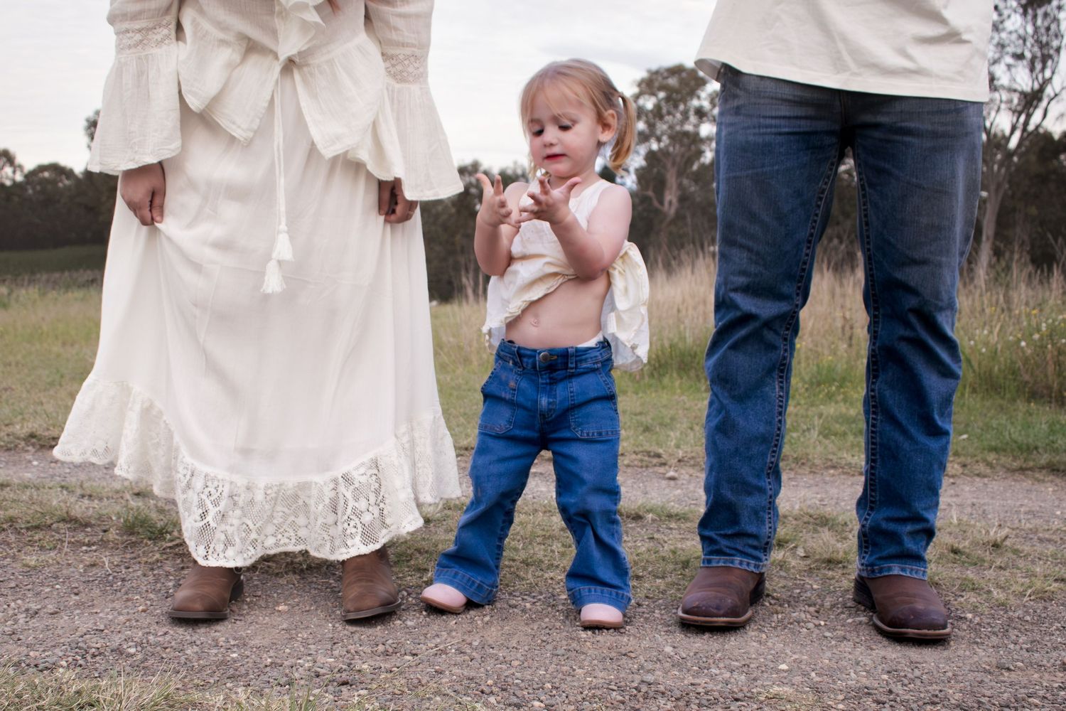 Mum, Dad, and toddler wearing cowboy boots on a dirt road with a grassy field during a golden hour newborn photoshoot Maitland NSW