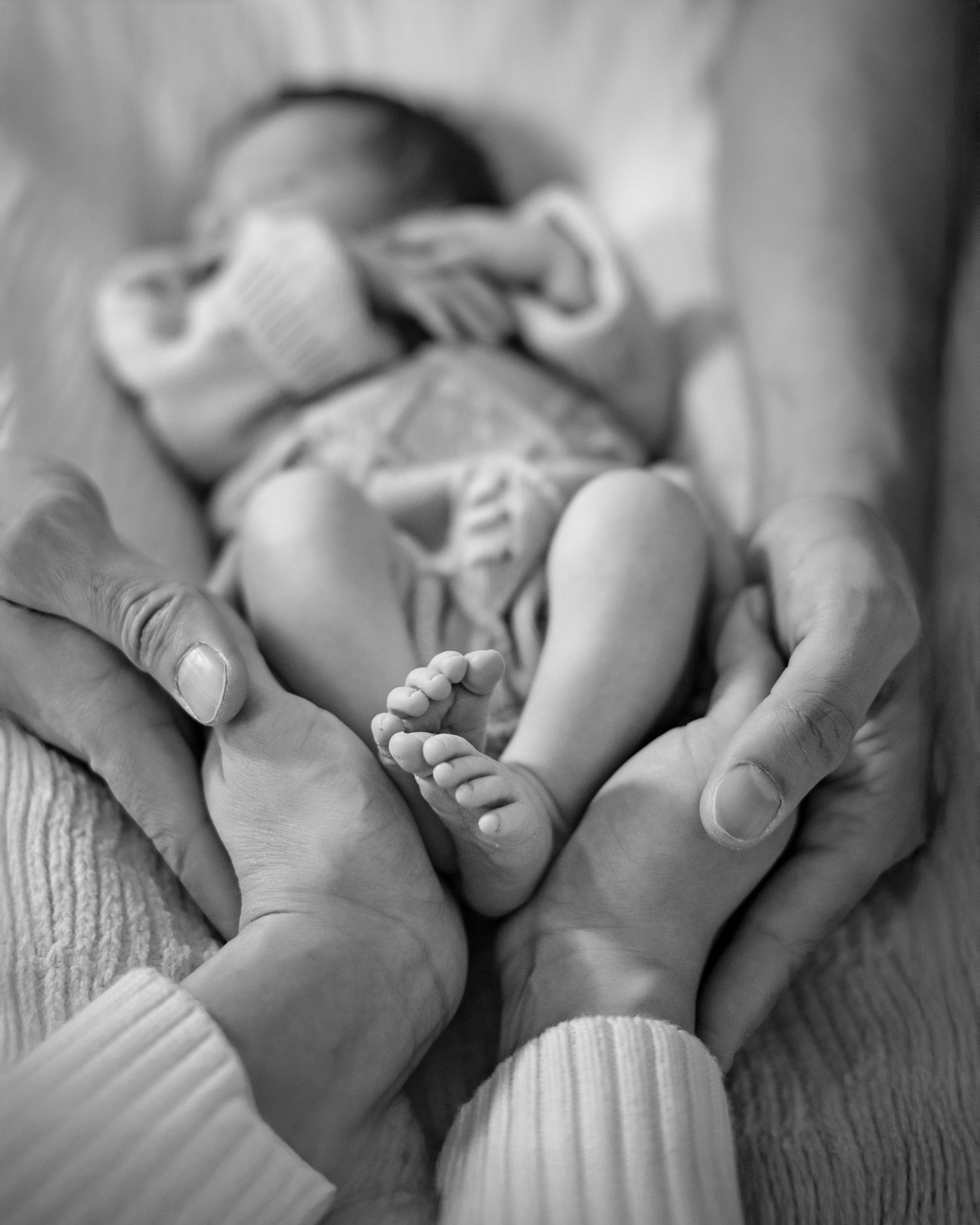 Parent's hands cradling their newborn daughter's feet.