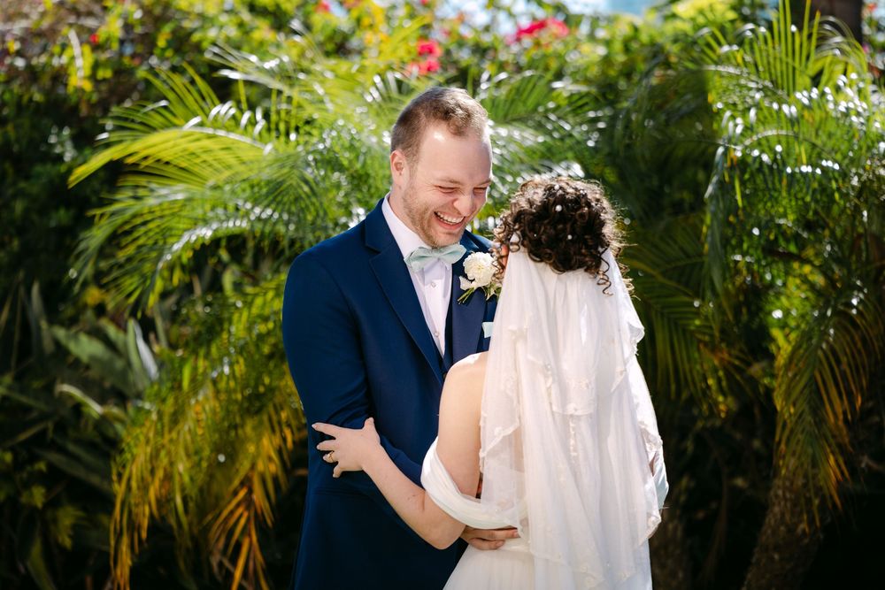 A wedding couple shares intimate moments among tropical palm trees in an outdoor garden setting.