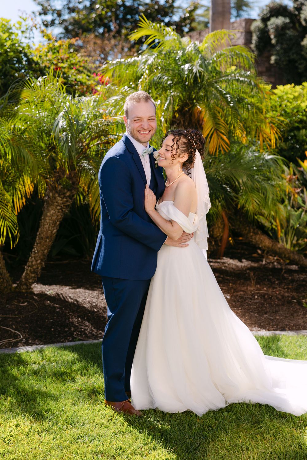 Newlyweds share romantic moments in a garden surrounded by palm trees and greenery.