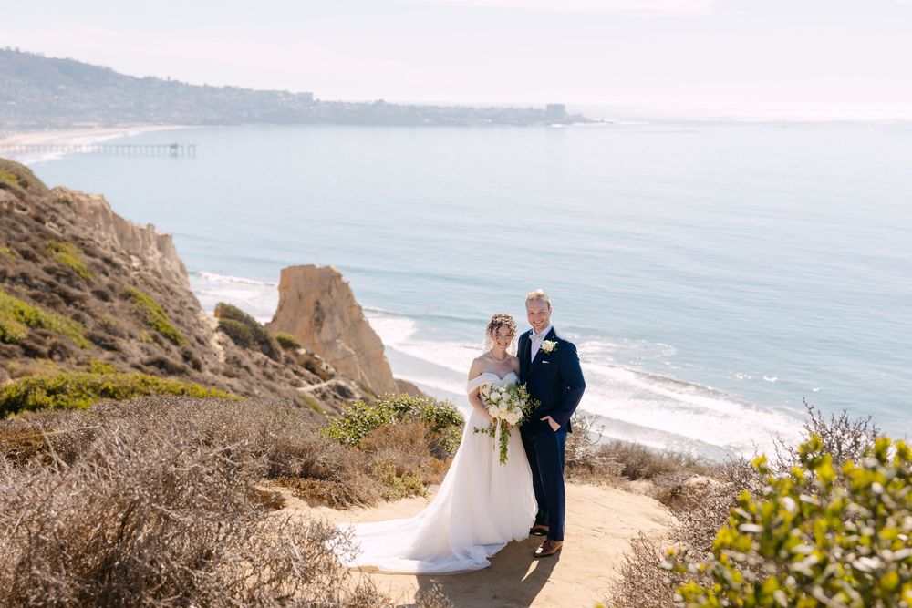 A scenic coastal wedding photoshoot with cliffs and ocean views at sunset.