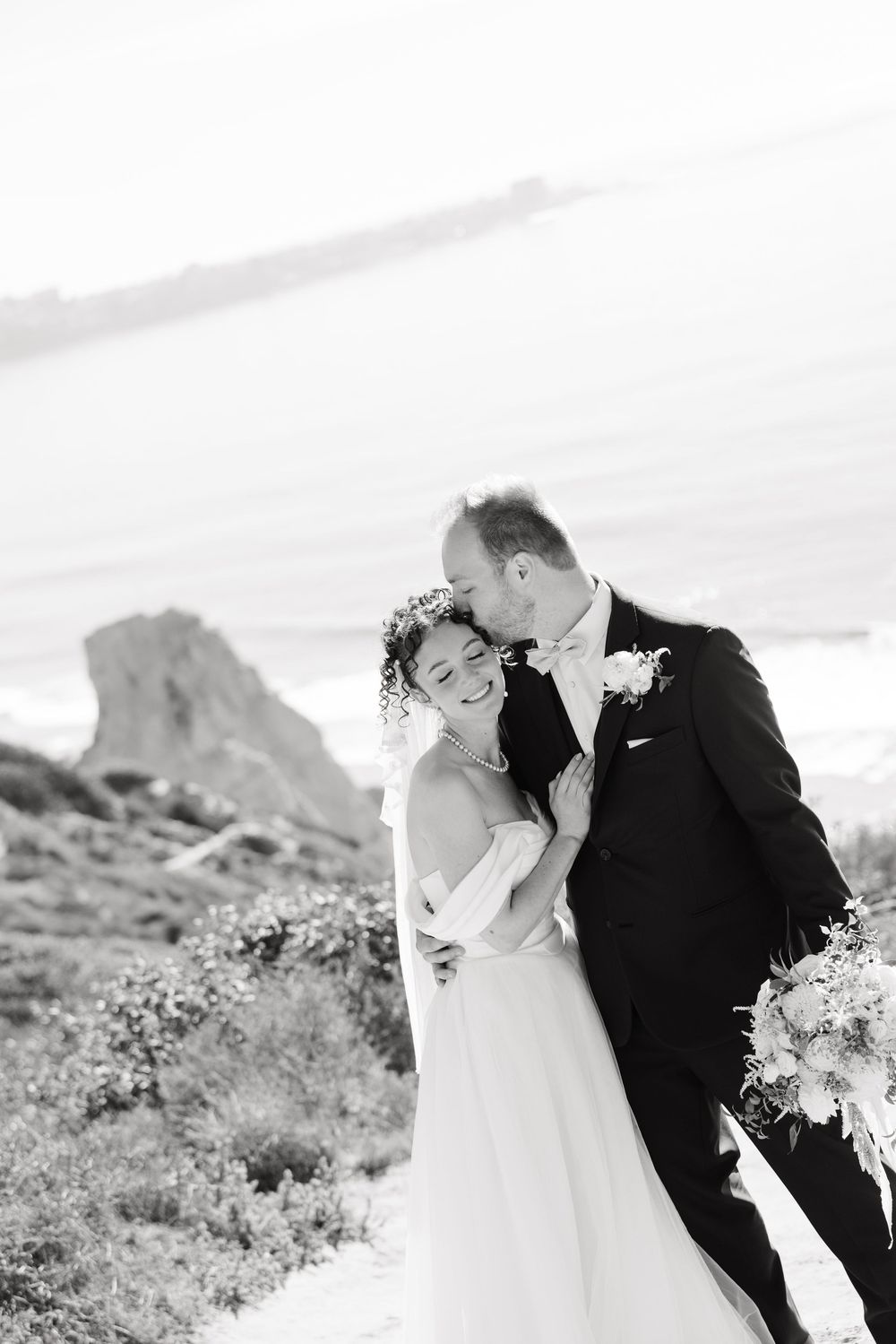 A romantic black and white wedding portrait series showing tender moments between newlyweds in a desert landscape.