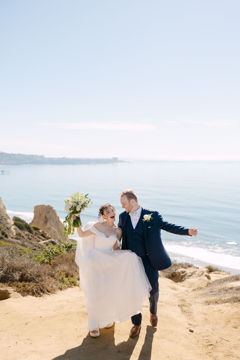 A couple shares a romantic moment on a scenic coastal cliff overlooking the ocean on their wedding day.