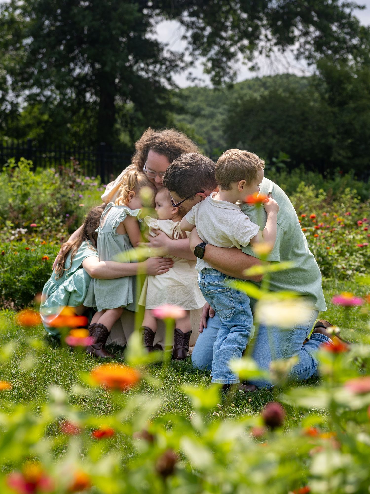 Family hugging in a lush garden surrounded by colorful flowers and green trees on a warm day.