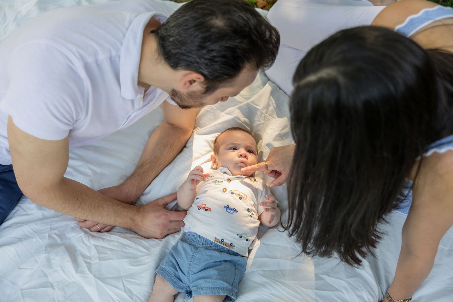 Parents lovingly gazing at their newborn baby lying on a white bed.
