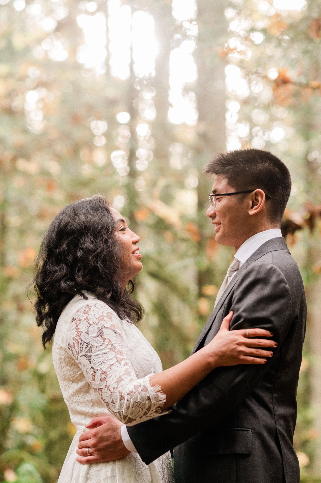 A wedding couple embraces in a dreamy forest setting with soft bokeh lighting and autumn colors on the Grand Forest West trail on Bainbridge