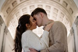Couple sharing a romantic kiss under an elegant archway, dressed in cozy white sweaters.