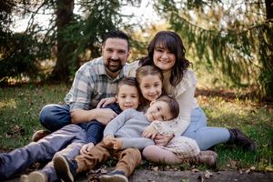 A family enjoys quality time together while laying on grass in a park during golden hour sunset.