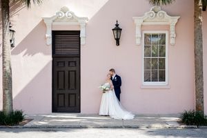 Bride and groom share a romantic moment beside a pink building with a dark door in Charleston, SC.