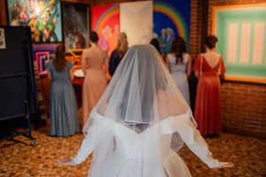 A bride in a flowing white veil and gown stands in a brick-walled venue during a wedding celebration.