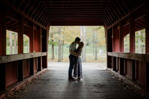 A silhouetted couple shares a romantic moment inside a long covered wooden bridge during autumn.