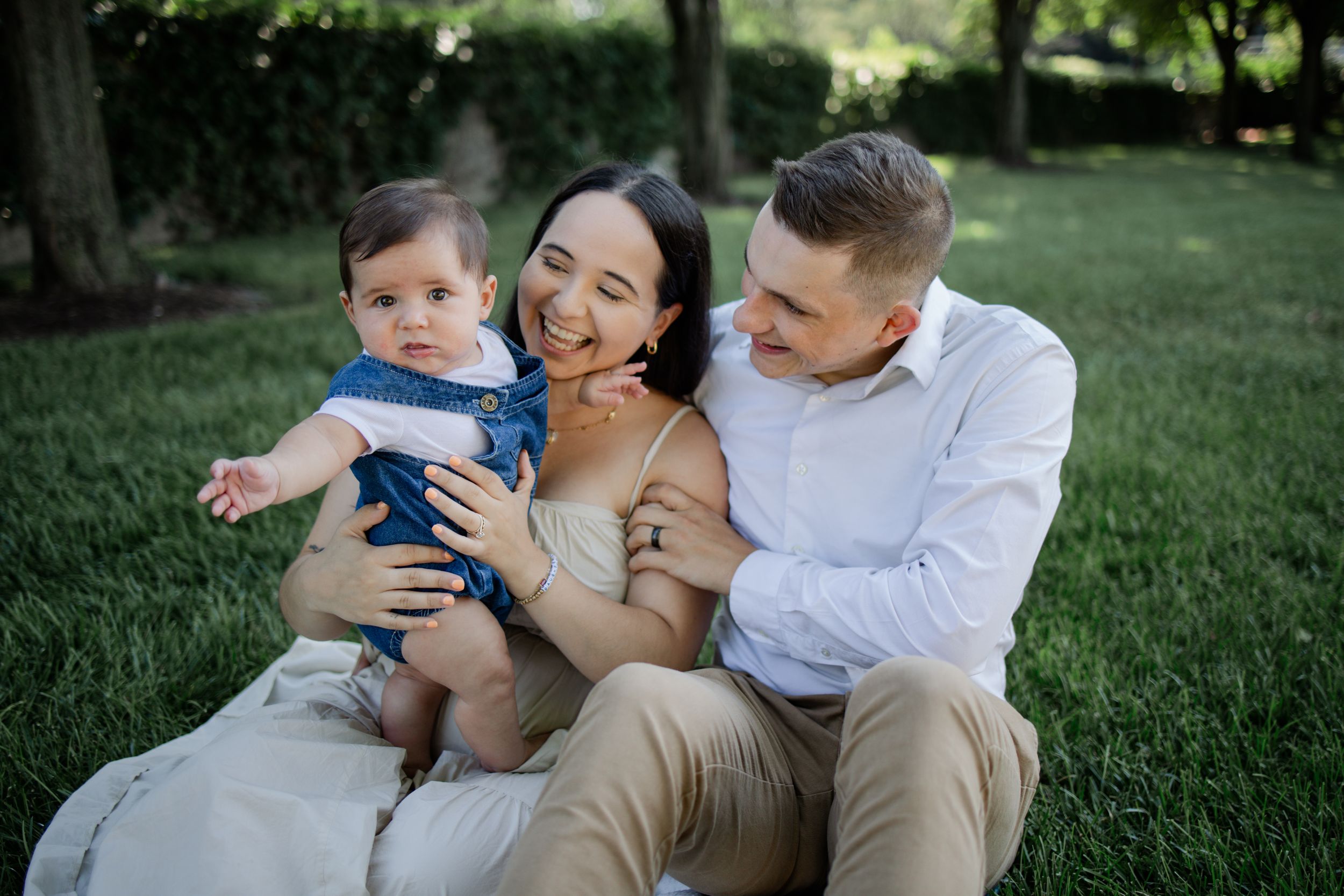 A family sits together on grass during a casual outdoor photo session in a park.