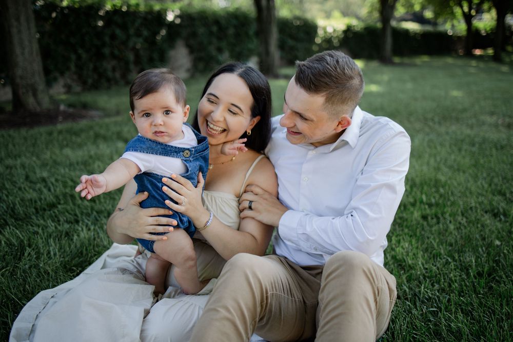 A family sits together on grass during a casual outdoor photo session in a park.