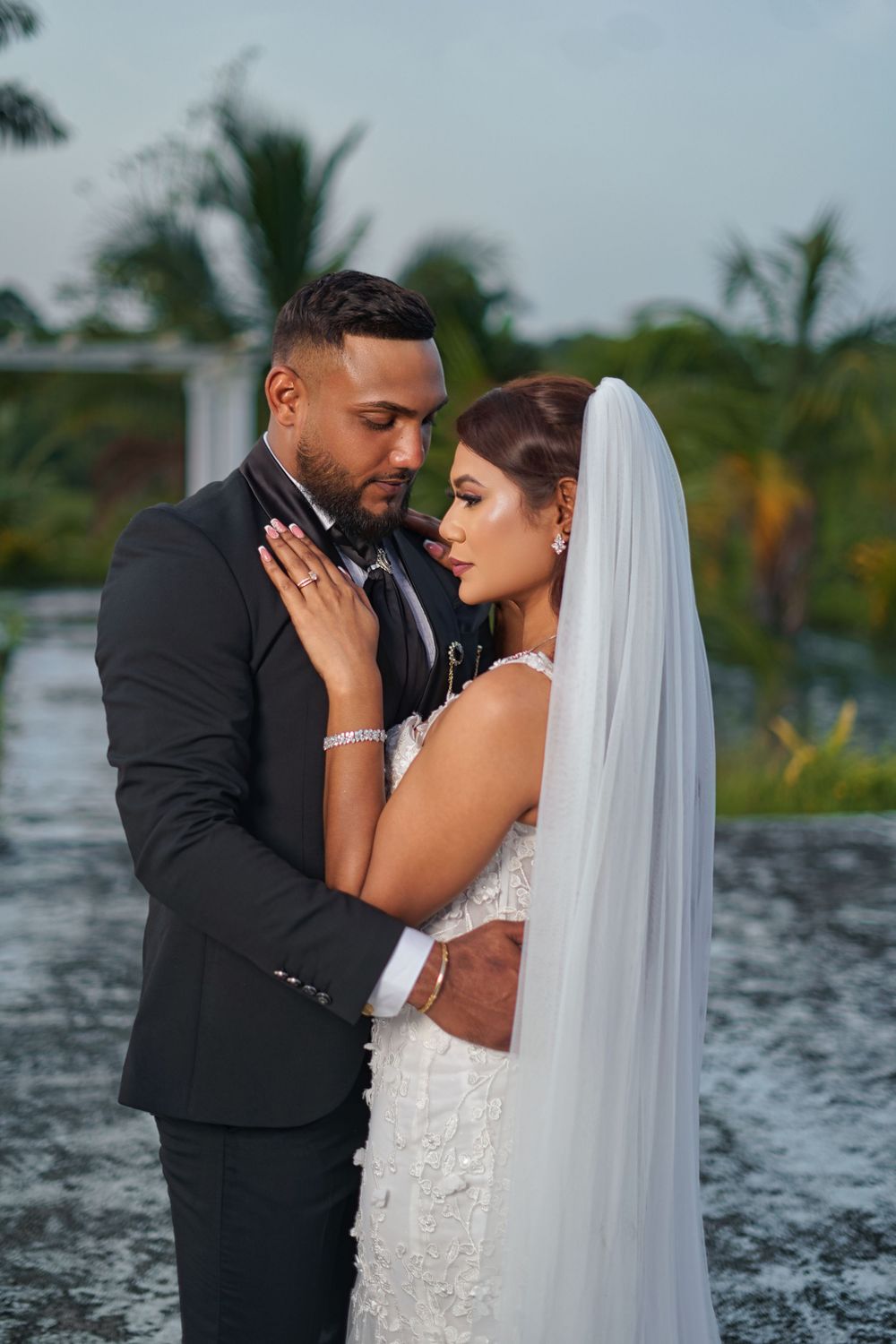 A romantic wedding couple shares intimate moments in a tropical setting with palm trees and water in the background.