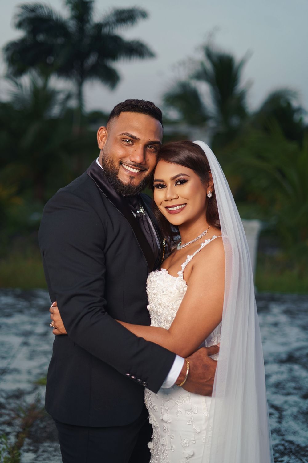 A joyful couple shares romantic moments during their tropical beach wedding photoshoot with palm trees in the background.