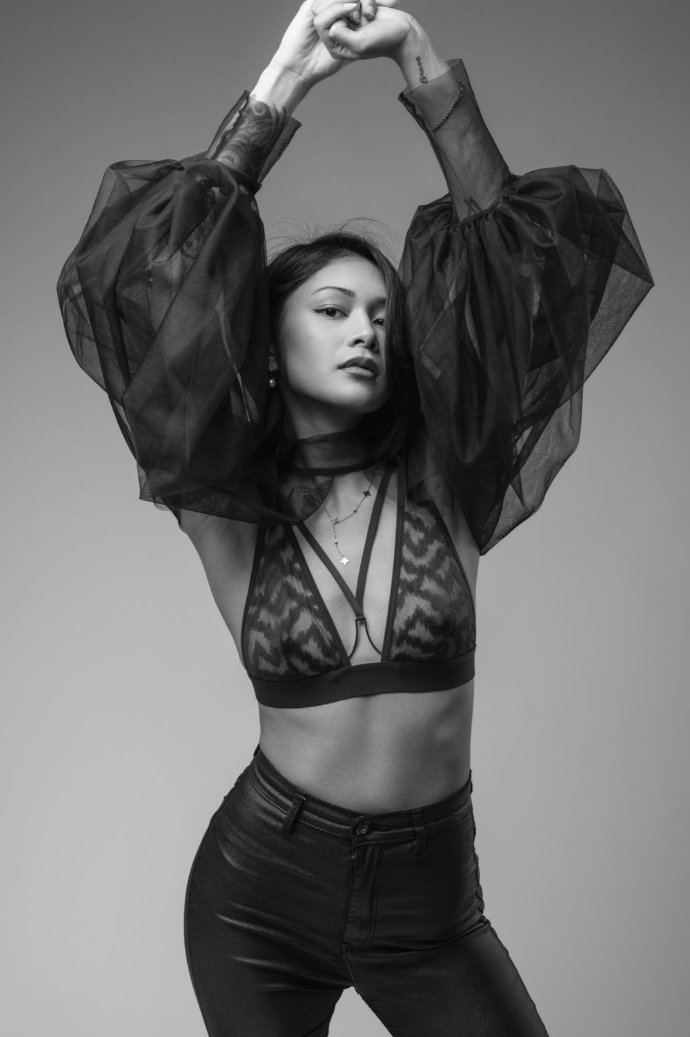 Black and white fashion portraits show a model in sheer black clothing striking dynamic poses against a plain backdrop.