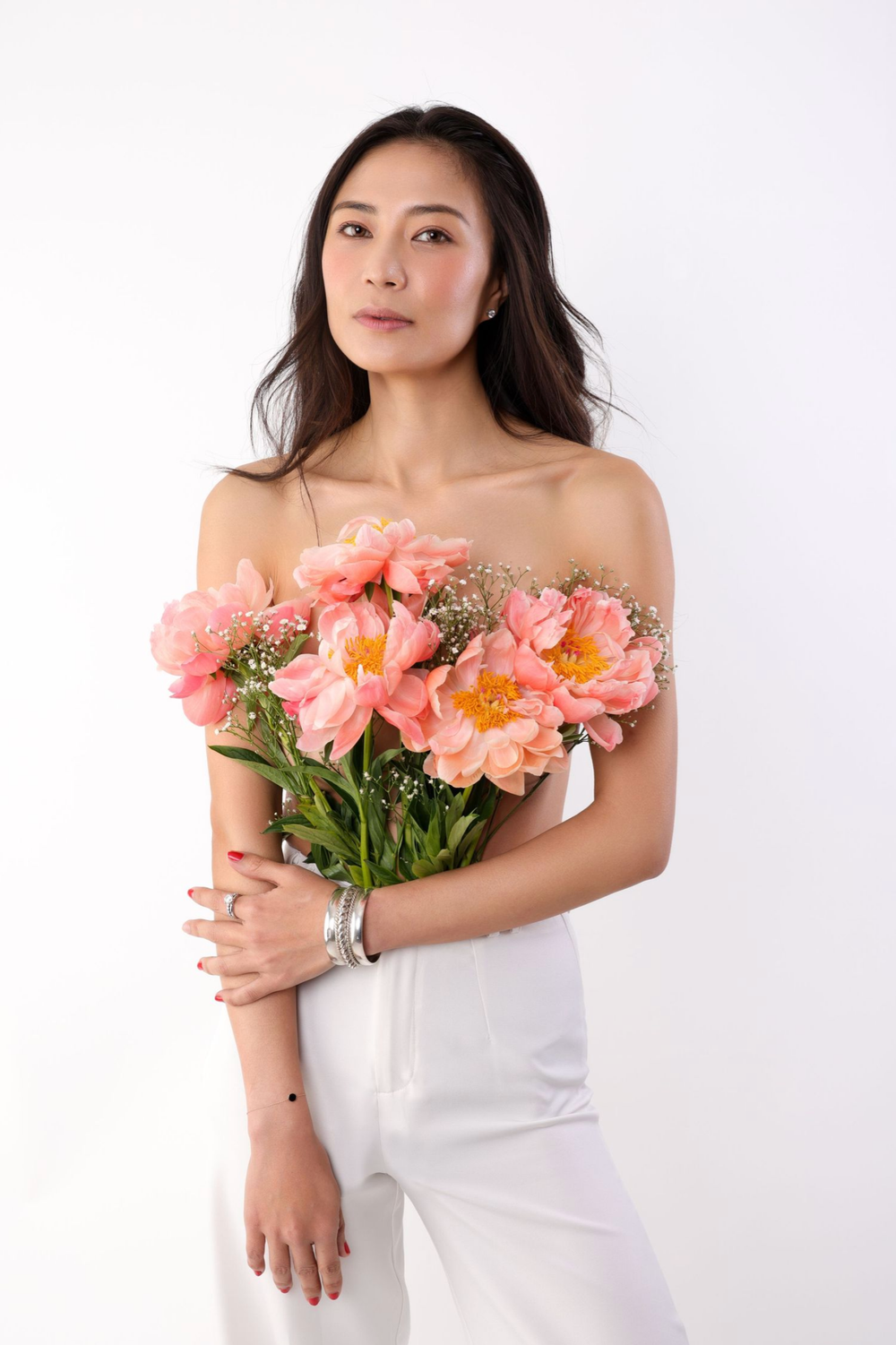 A person in white holding a bouquet of coral-colored peonies against a light background in a series of elegant poses.