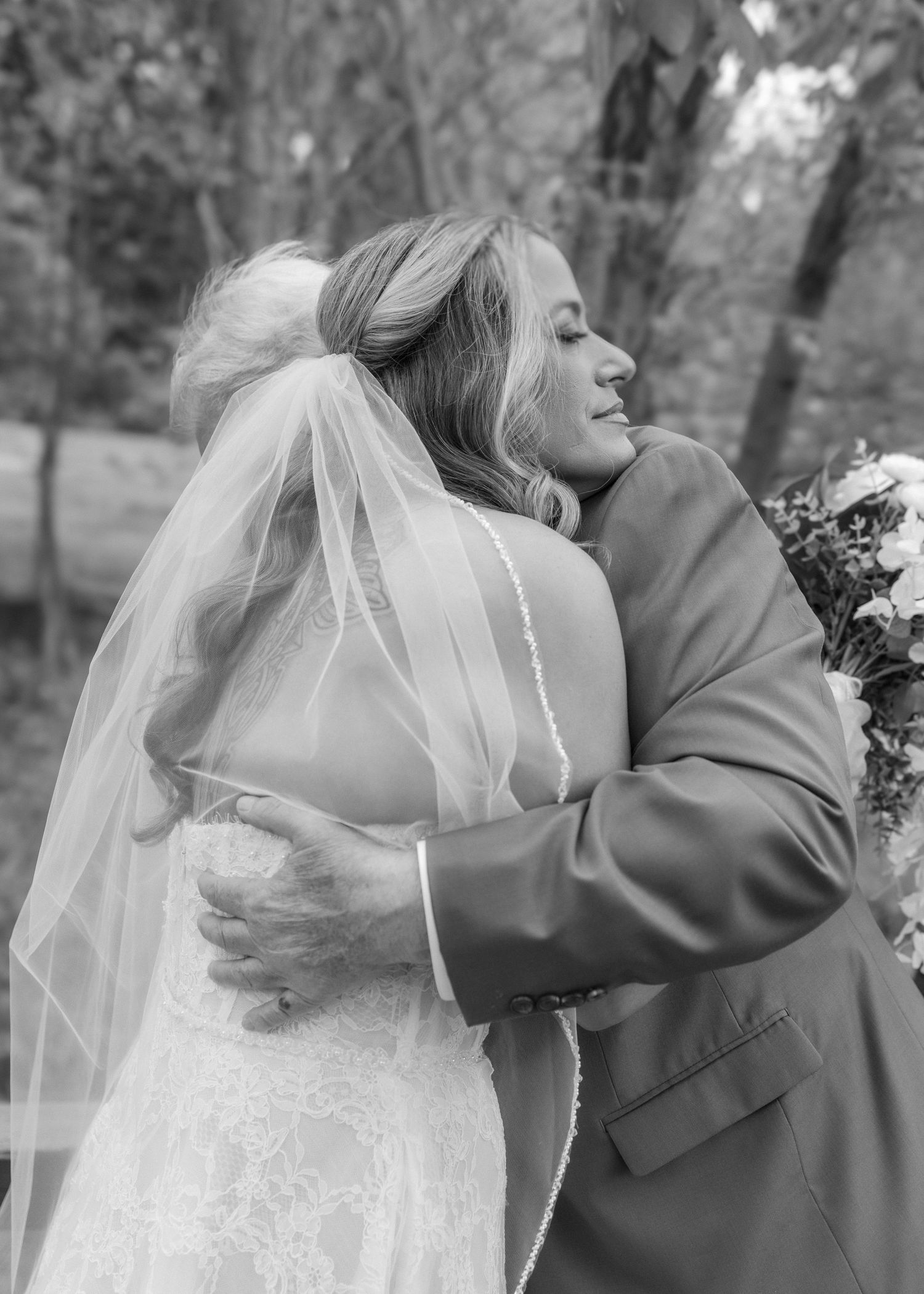 Bride in lace gown and veil shares an emotional hug with a guest during wedding celebration.