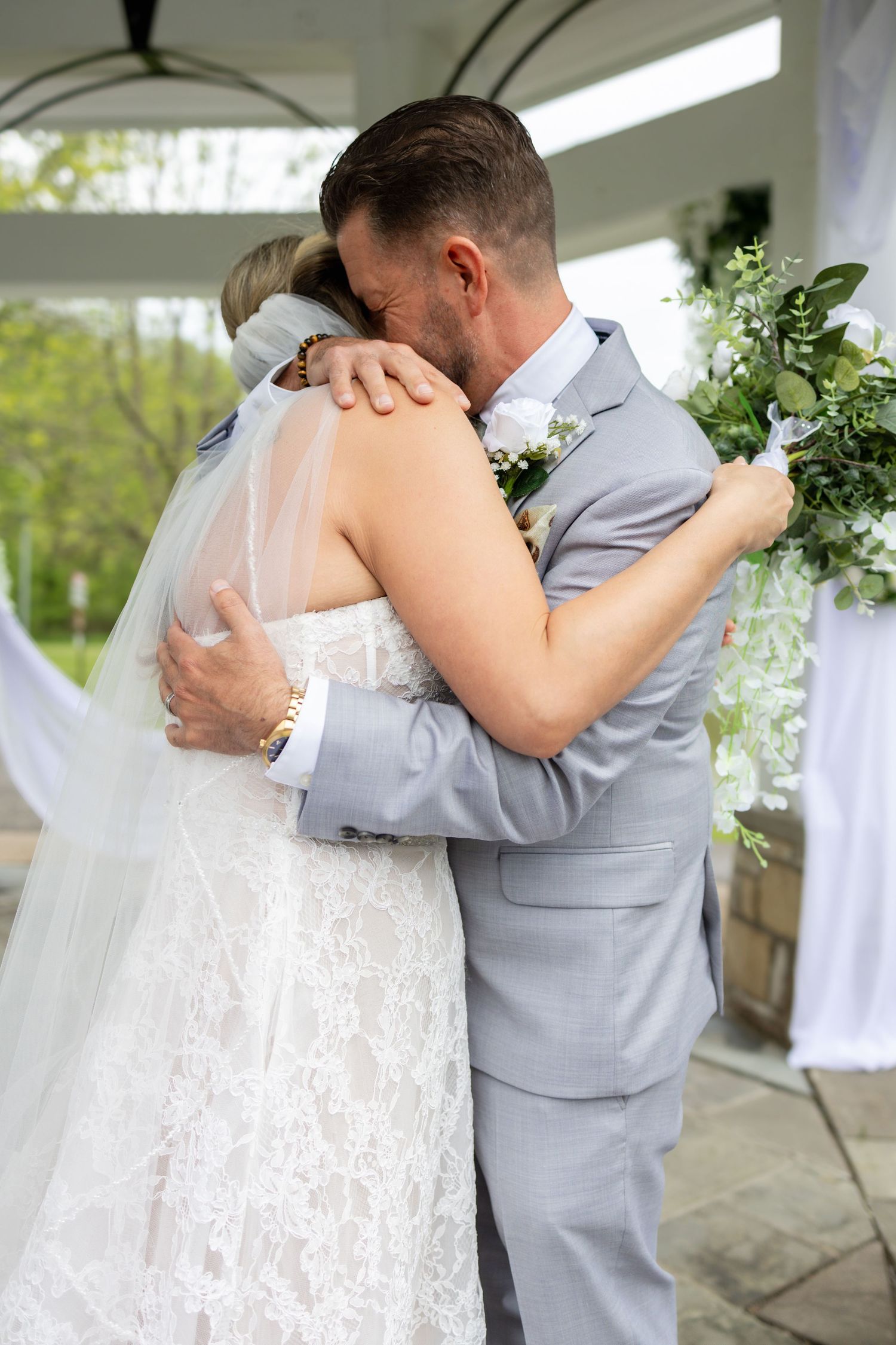 Bride and groom share a heartfelt embrace during their outdoor wedding ceremony under a white gazebo.