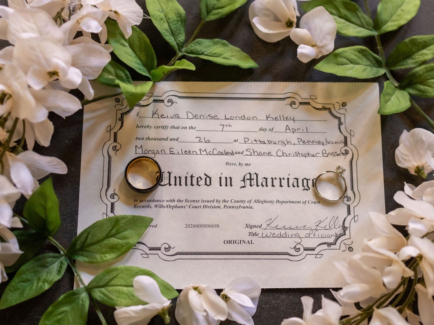 Gold wedding rings resting on a United in Marriage certificate surrounded by white flowers.