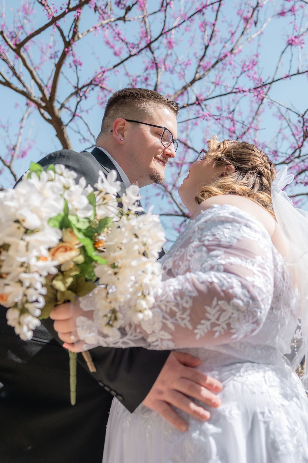 Bride and groom sharing a romantic moment under a blooming cherry blossom tree, bride holding white flower bouquet.
