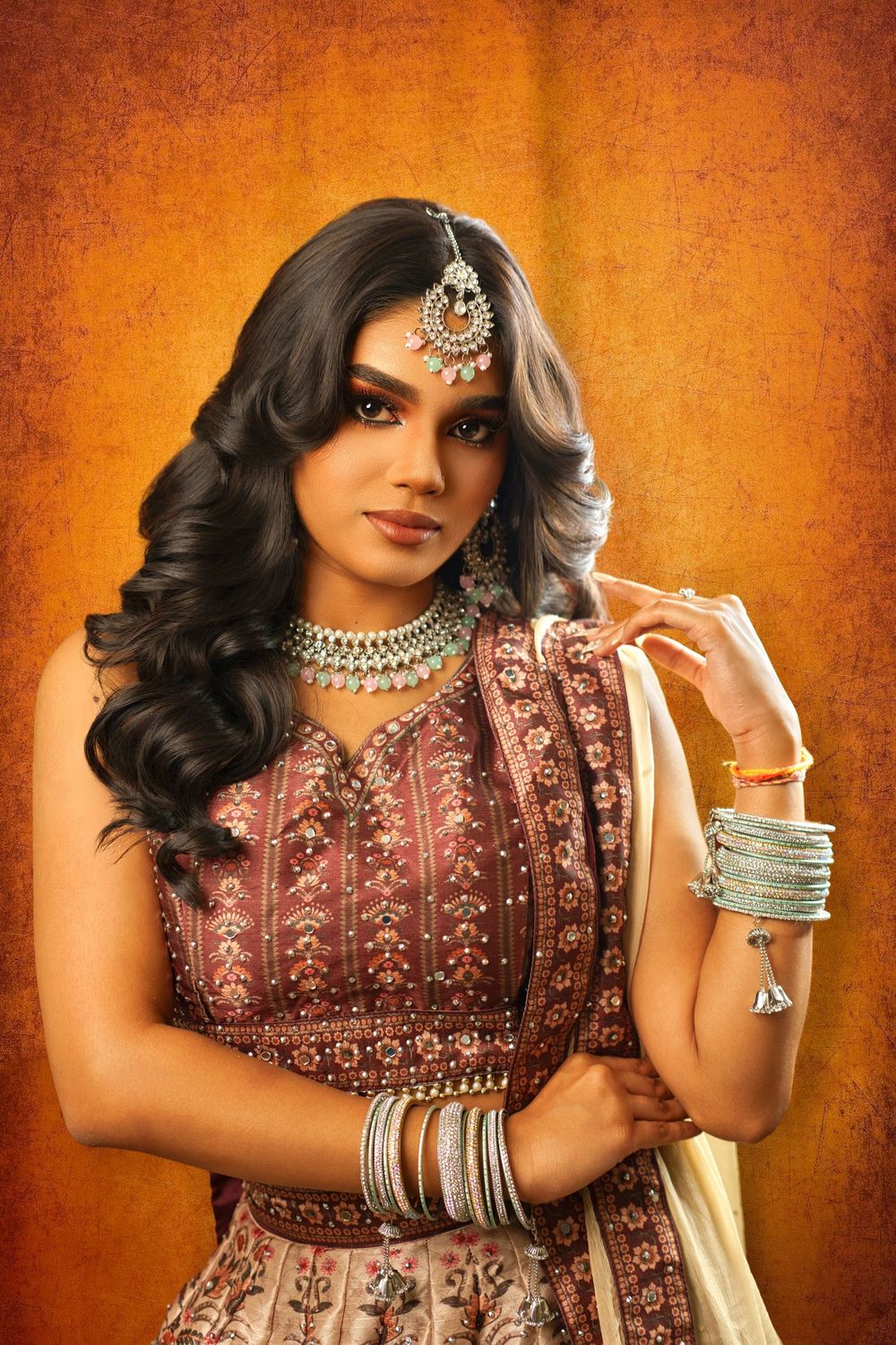 Elegant Indian bridal portraits featuring burgundy embroidered lehenga and statement jewelry against orange background.