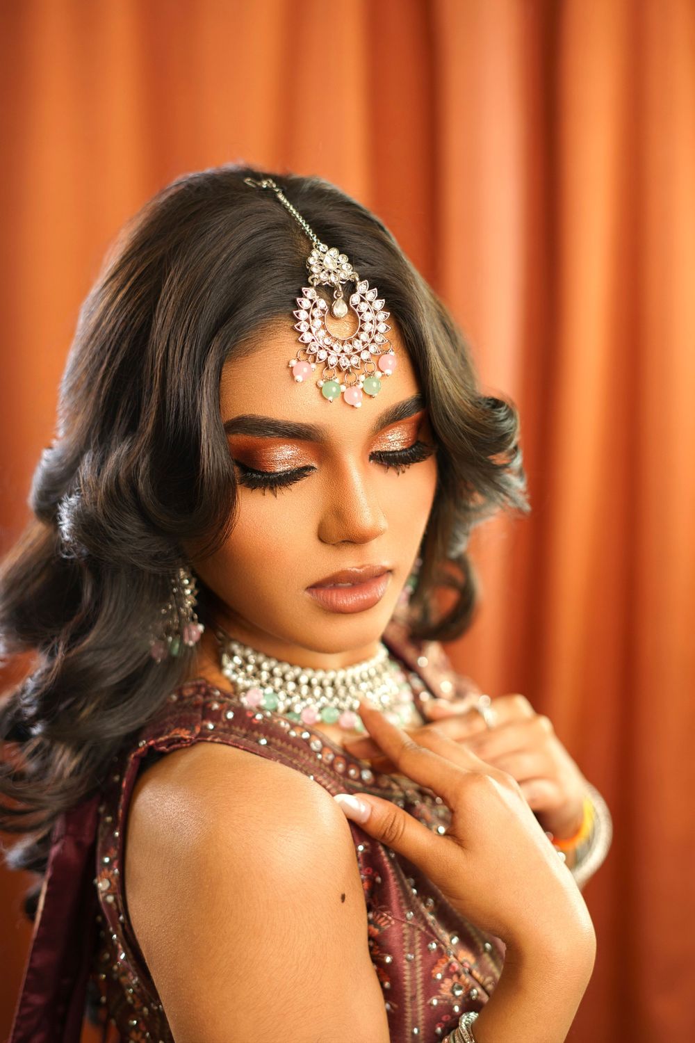 Traditional Indian bridal jewelry and makeup details showcased against an orange curtain backdrop.