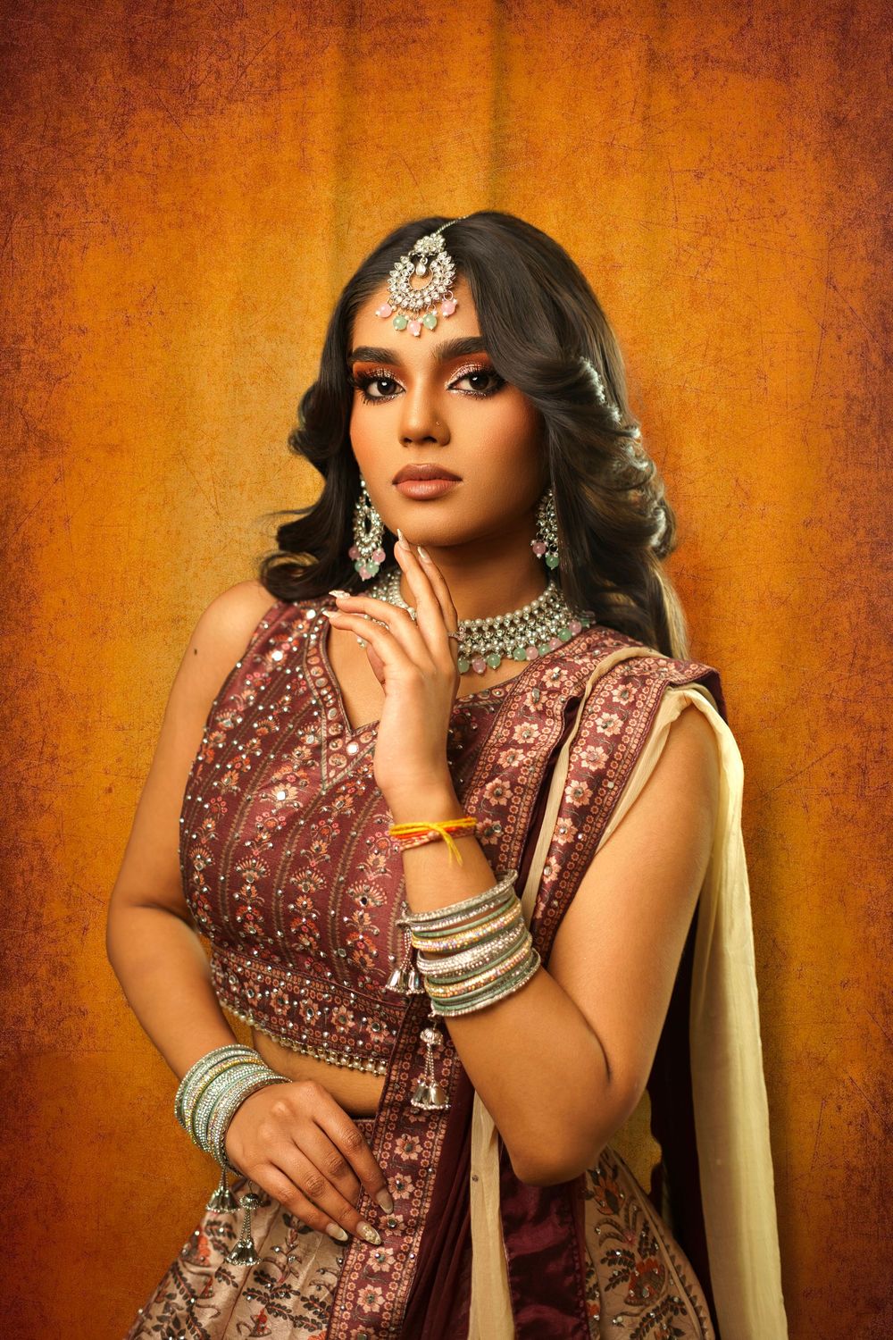 Traditional Indian bridal portrait featuring ornate jewelry and a dusty rose lehenga against a warm orange backdrop.