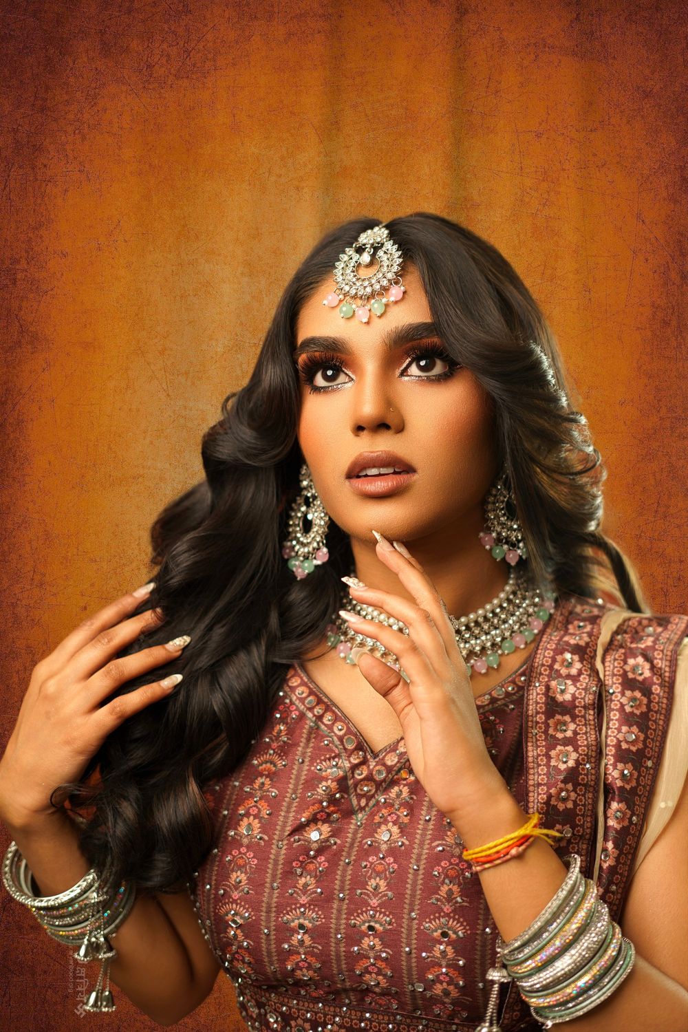 A glamorous fashion portrait showcasing intricate Indian bridal jewelry and a burgundy embroidered outfit against warm lighting.